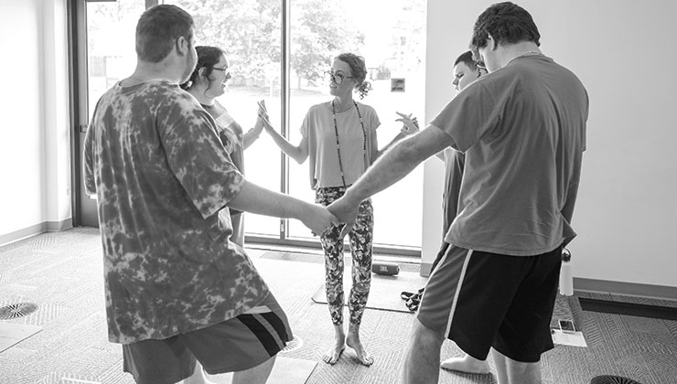 Community classes: participants standing in a circle holding hands with Sam in a sunlit studio